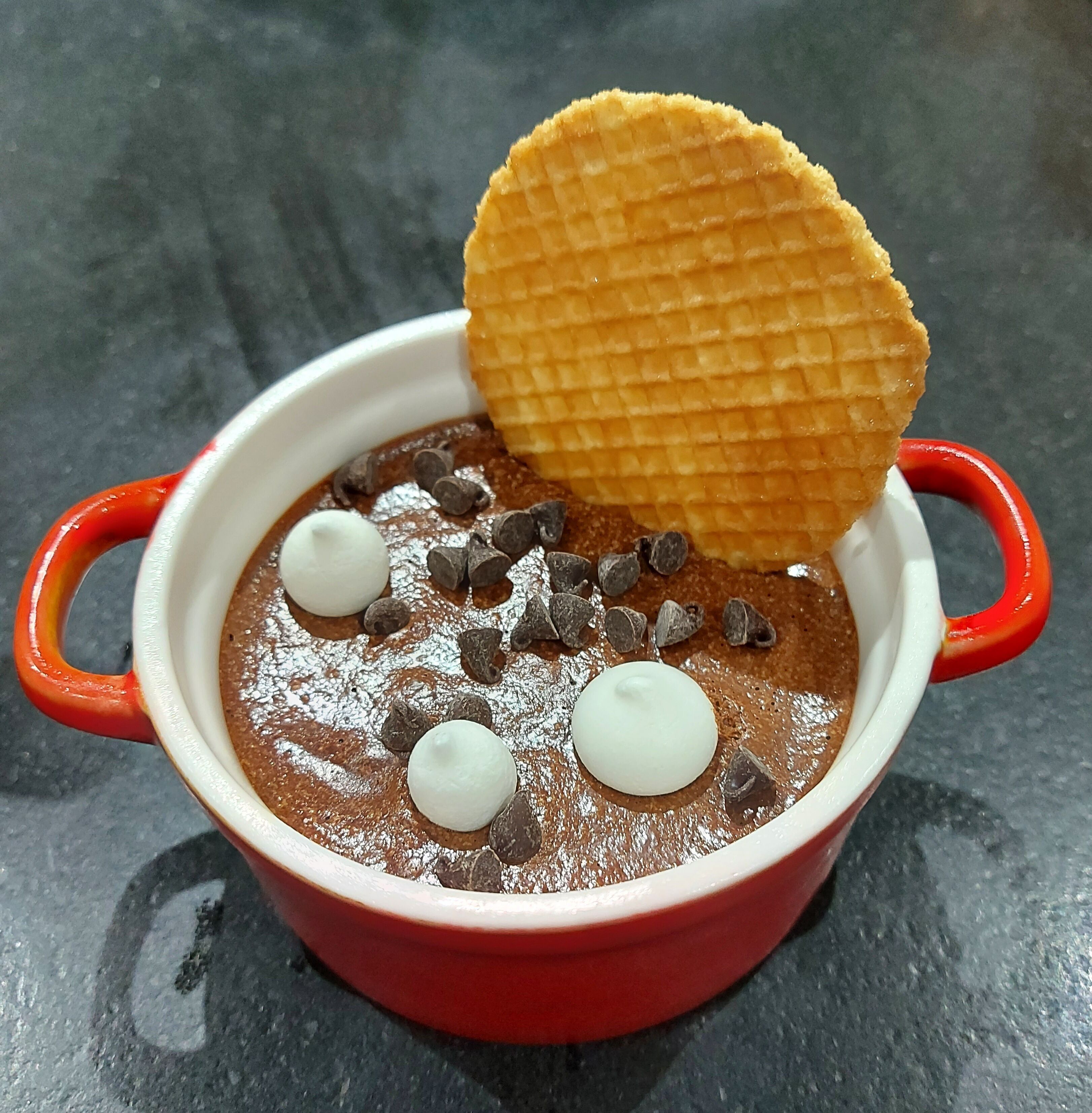Un bol de dessert au chocolat, garni de crème fouettée et de pépites de chocolat, accompagné d’une gaufre.