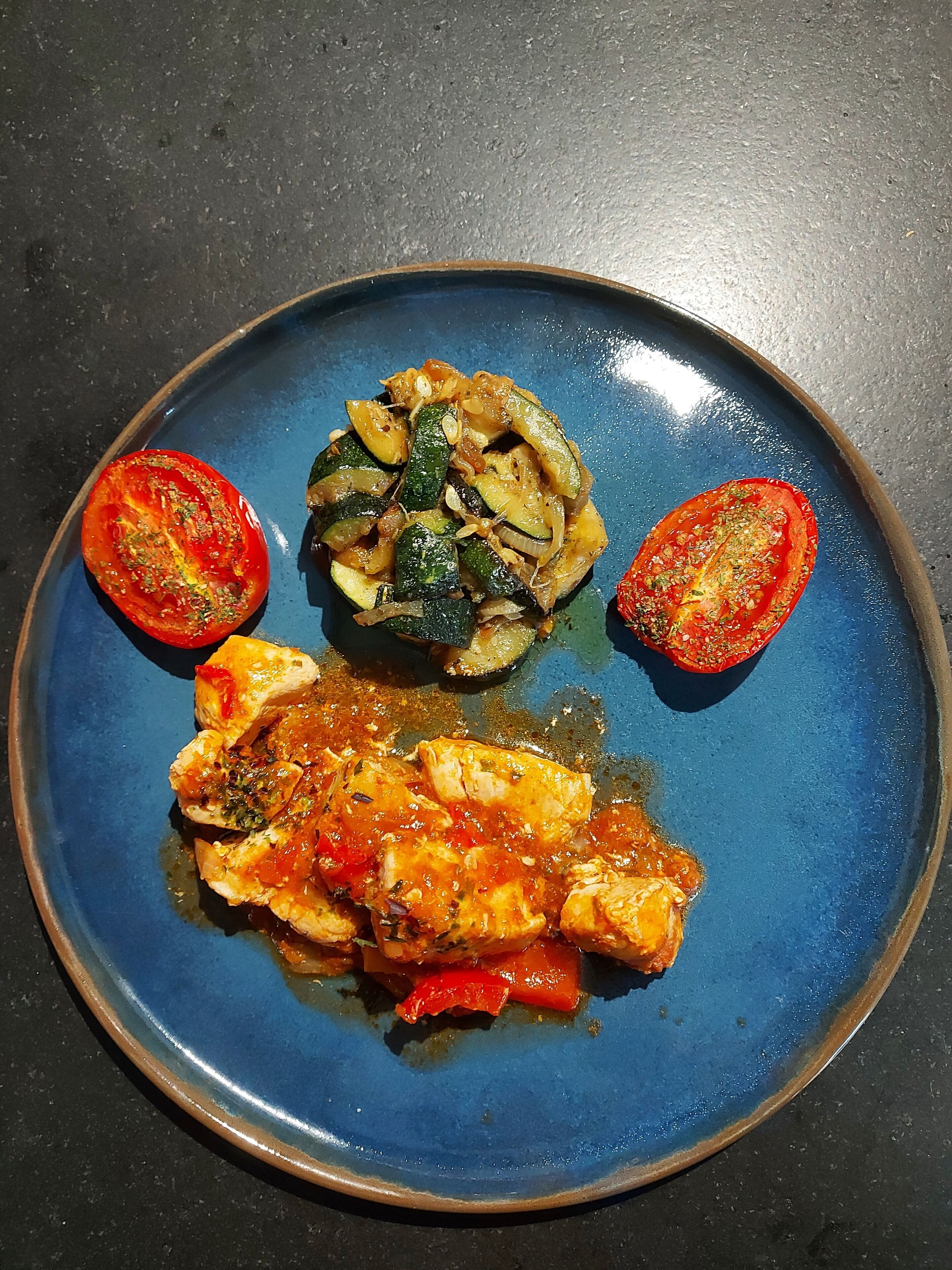 Un plato azul con un filete de pescado, rodajas de calabacín y tomates cherry.
