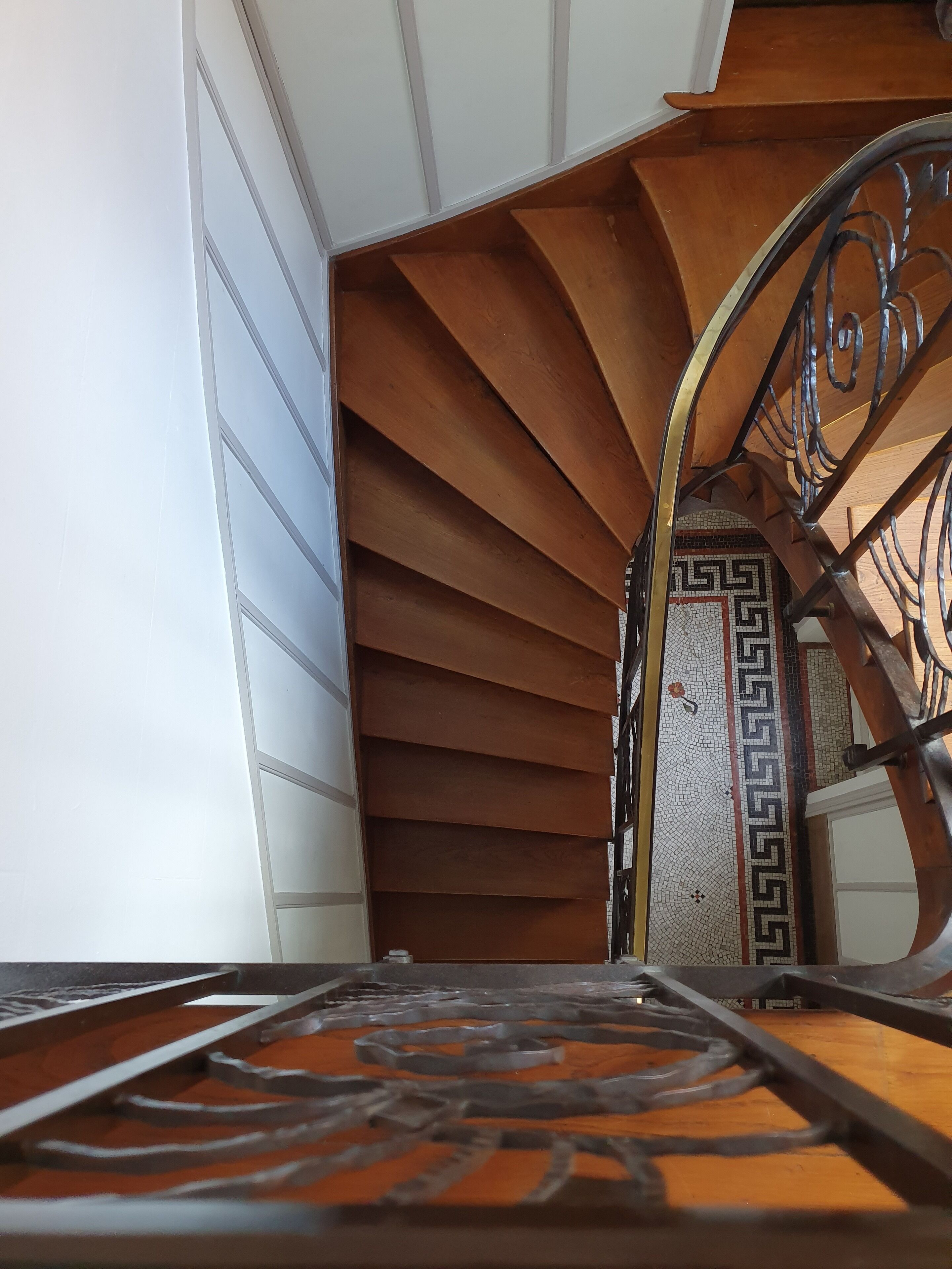 Un escalier en colimaçon avec un sol à motifs géométriques et une rampe en métal.