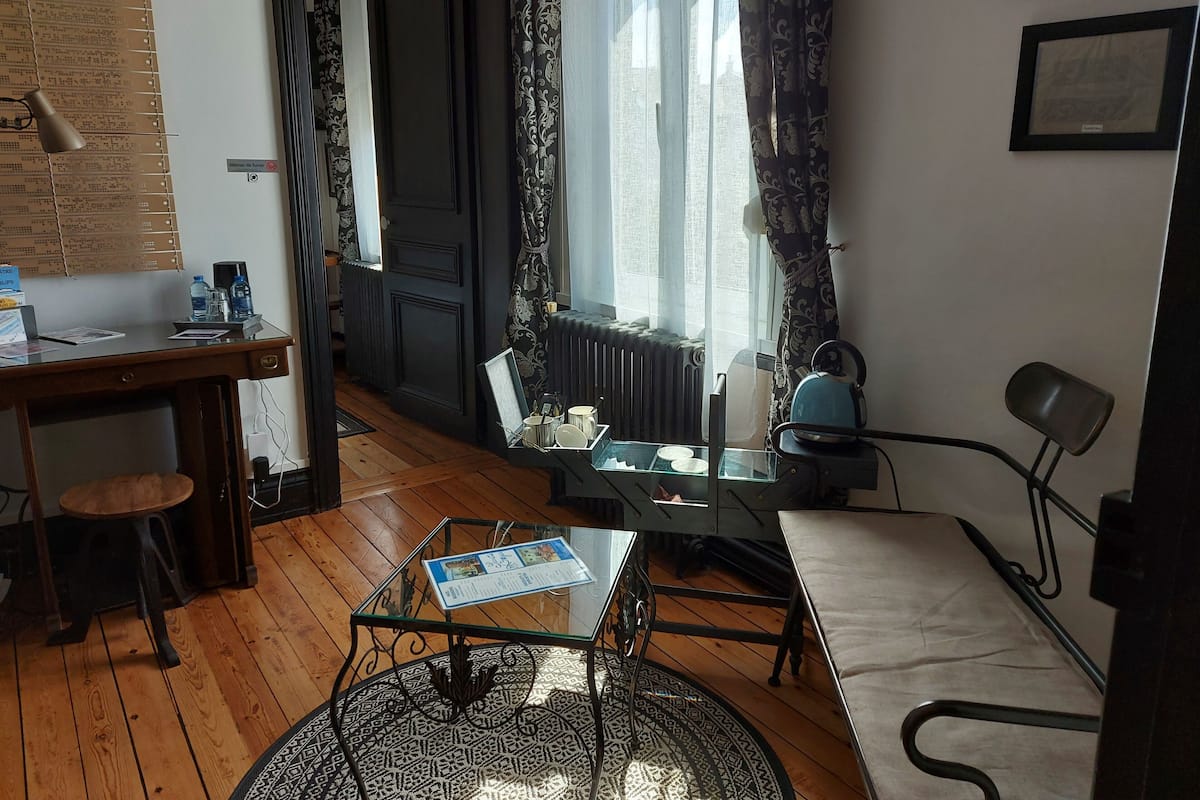 A cozy room with a wooden floor, a glass table, a chair, a radiator, and a window with curtains.