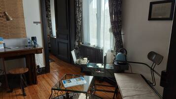 A cozy room with a wooden floor, a glass table, a chair, a radiator, and a window with curtains.