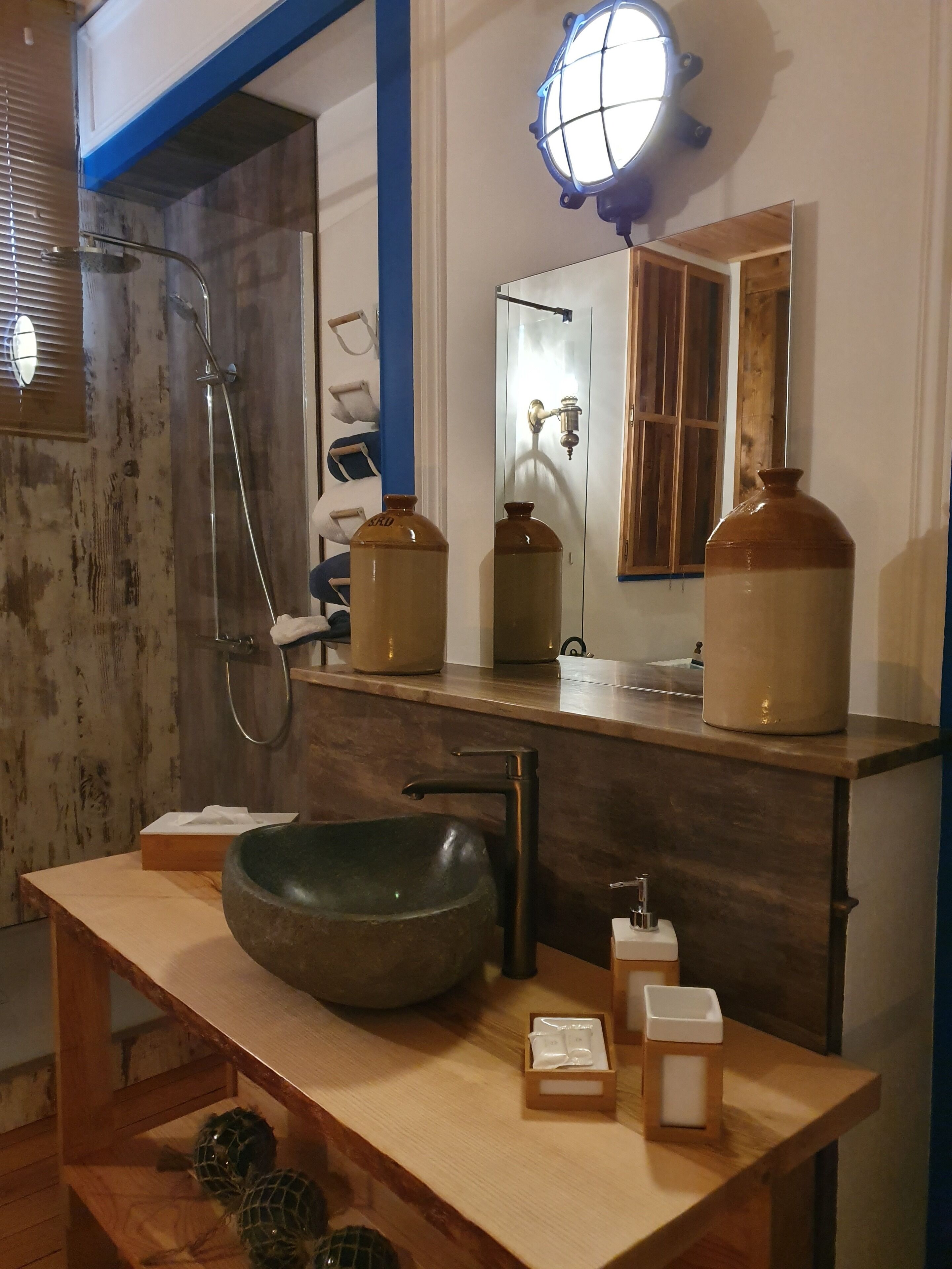 Un bagno con un mobile vanitario in legno, un lavabo a forma di grande ciotola, un soffione doccia a mano e uno specchio con un corpo illuminante sopra.
