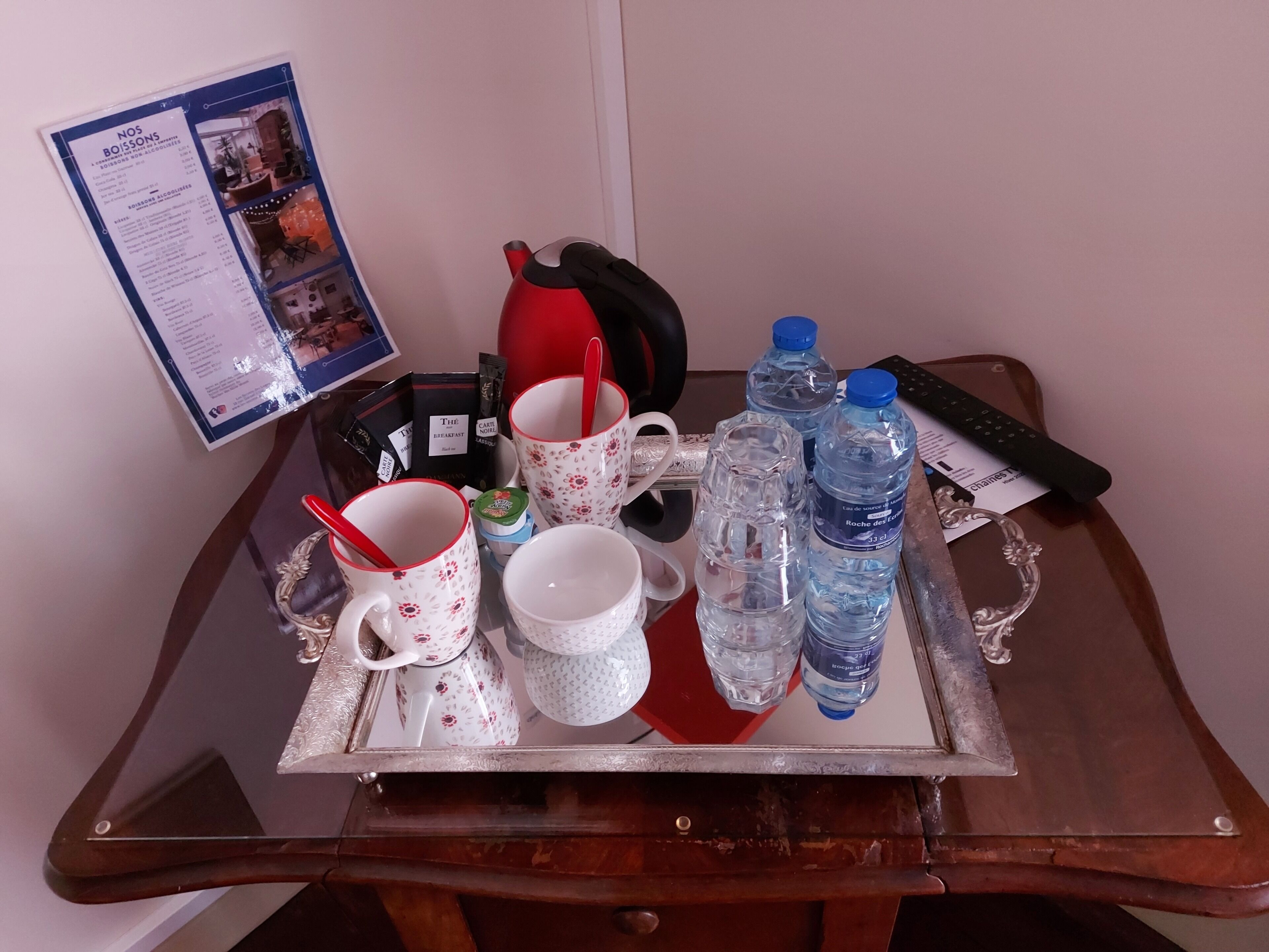 A tray with a teapot, cups, a kettle, and bottled water on a wooden table.