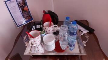 A tray with a teapot, cups, a kettle, and bottled water on a wooden table.