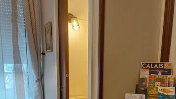 Ein Holzboden, eine weiße Toilette, ein gerahmtes Bild an der Wand und ein Regal mit Büchern und Zeitschriften.