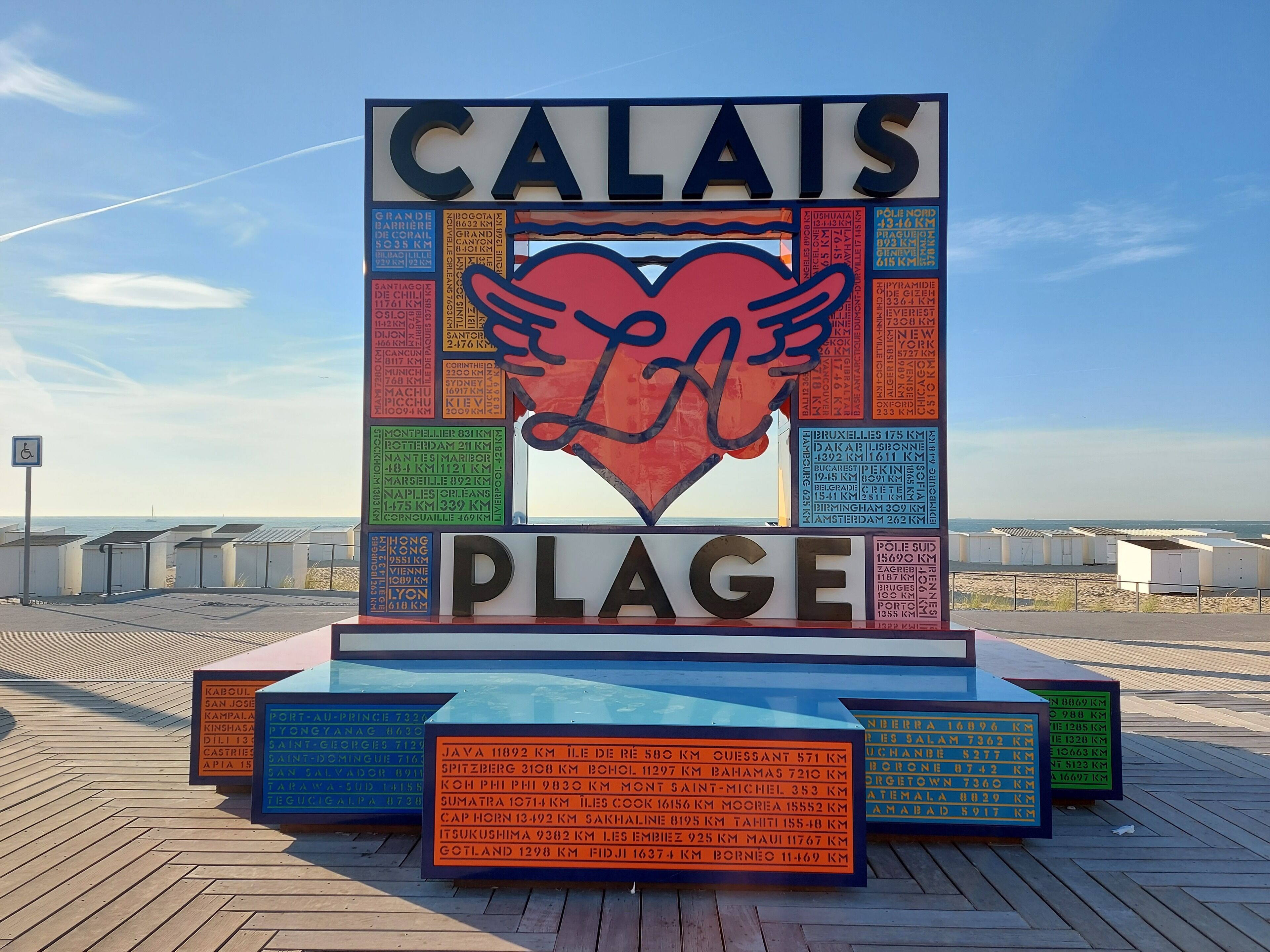 Un muelle con un cartel grande que muestra distancias a ciudades y un corazón con alas.