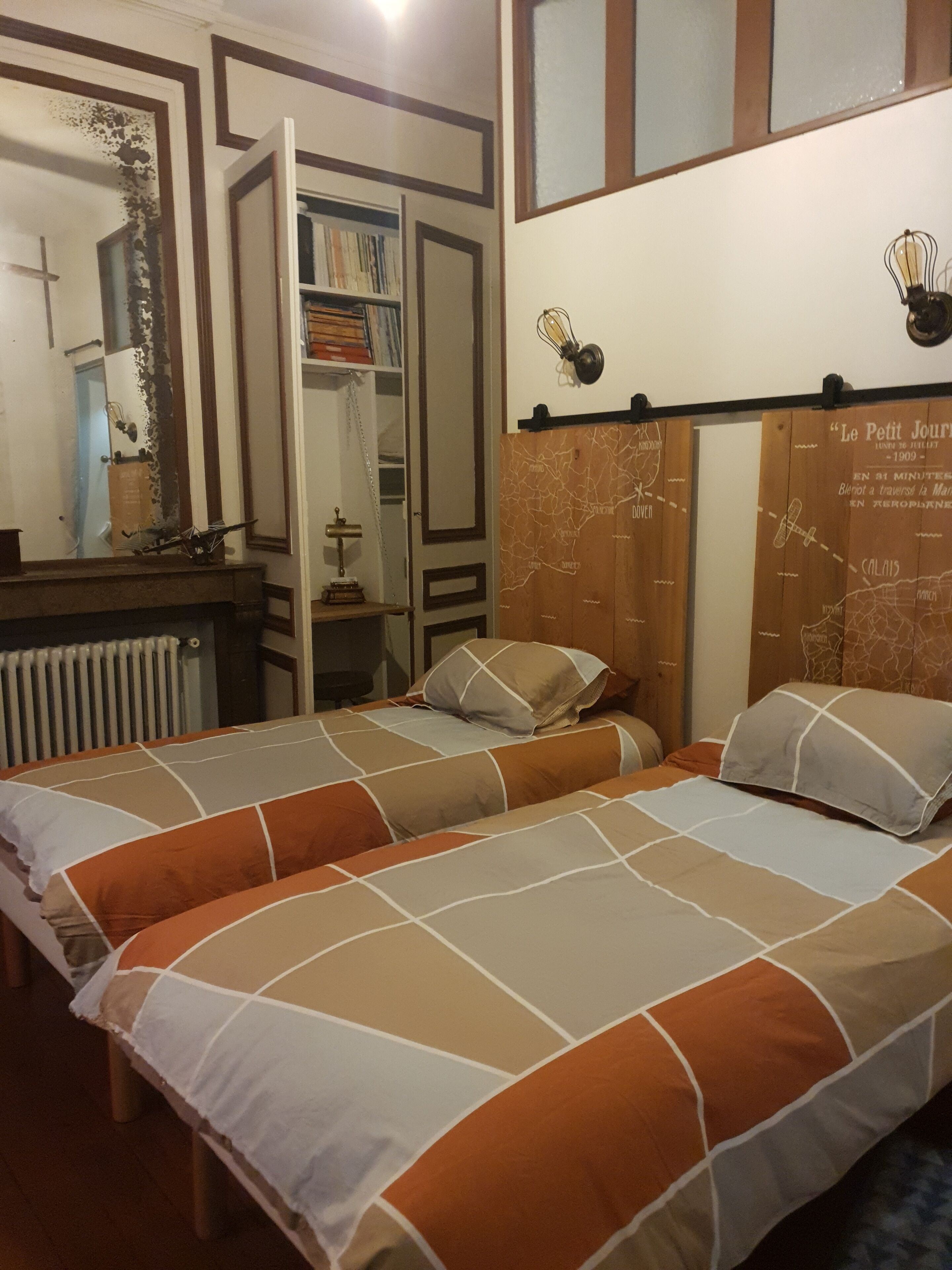 A bedroom with two beds, a bookshelf, a radiator, and a map on the wall.