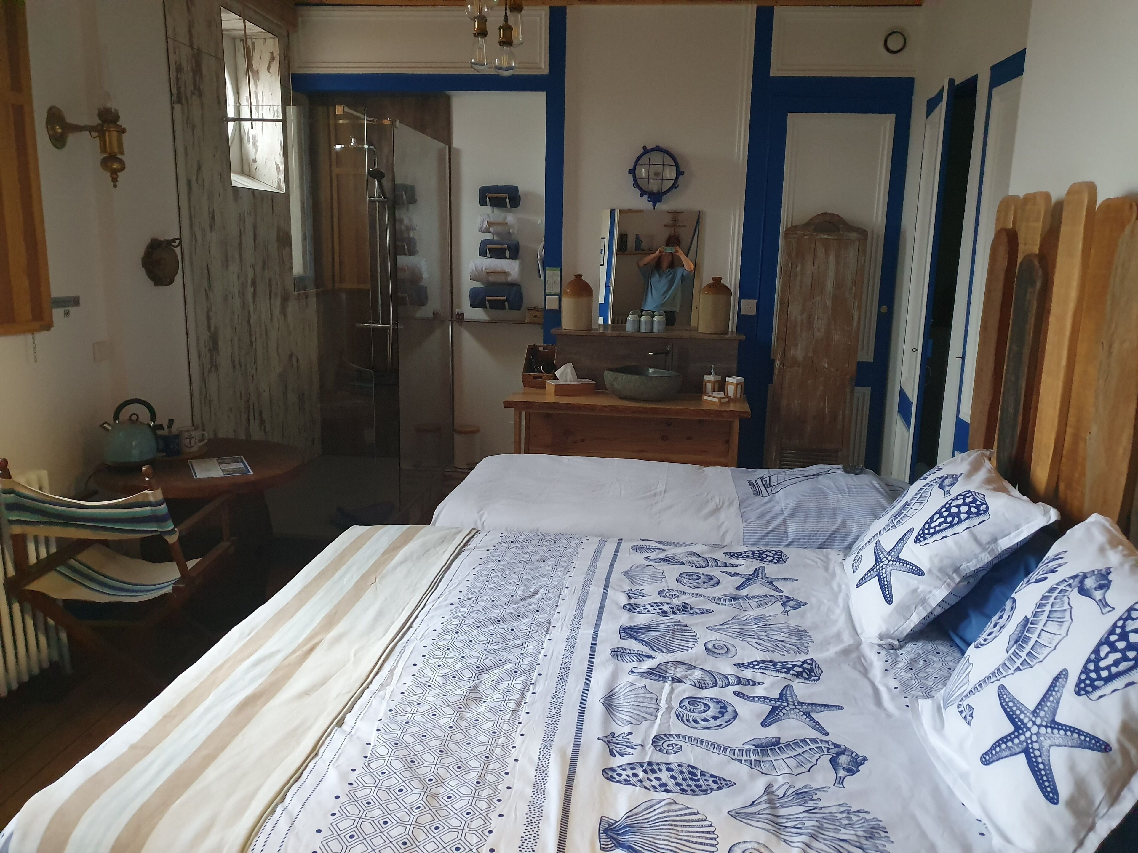 A bedroom with a bed, a wooden nightstand, a mirror, and a bathroom visible through a glass door.