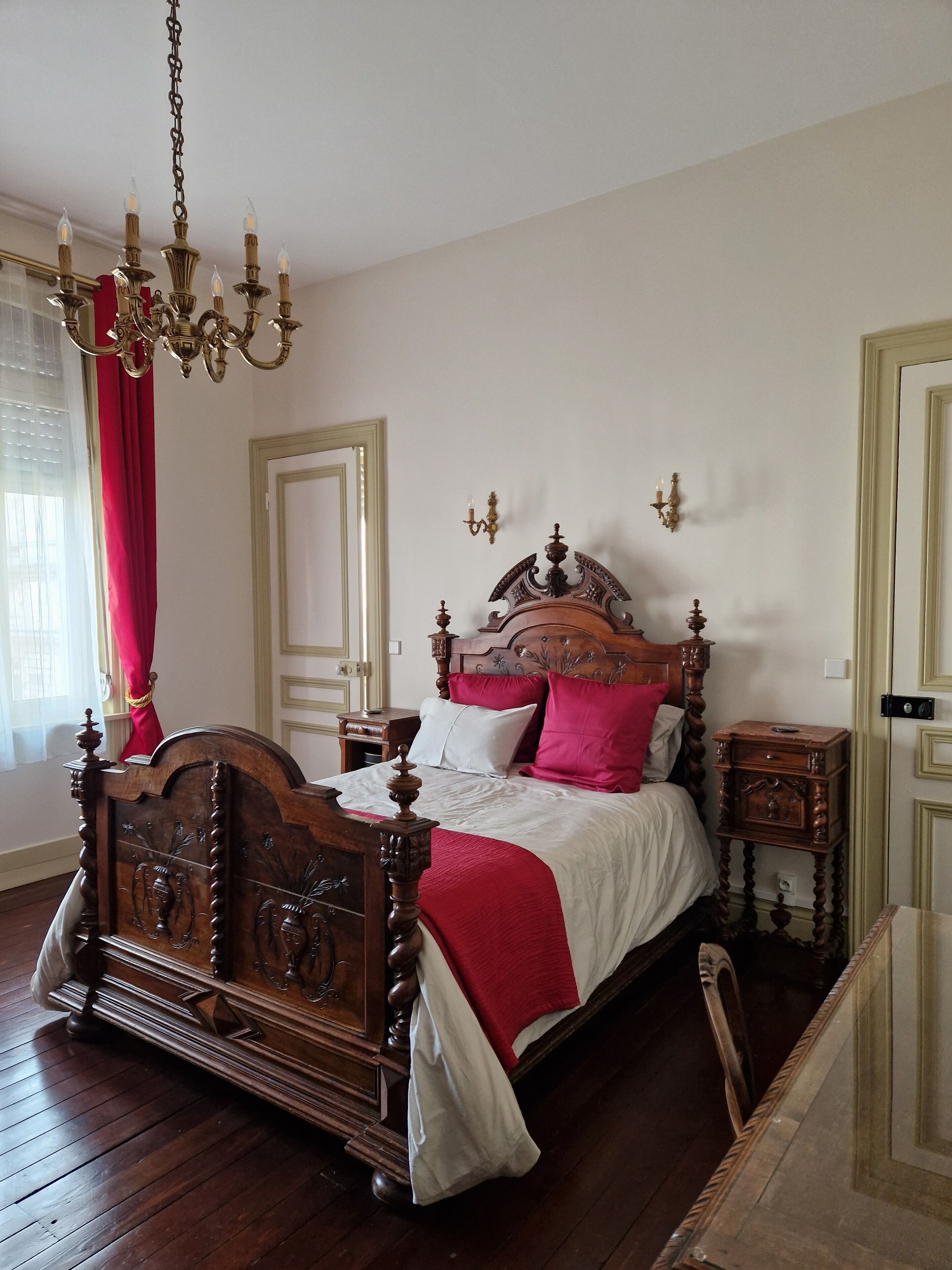 Un dormitorio clásico con una cama de madera con dosel, una araña y una cortina roja.