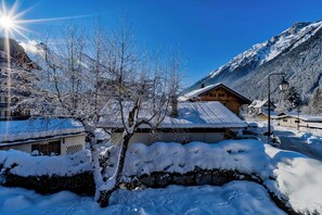 A snow-covered mountain village with wooden houses, a clear sky, and a visible street.