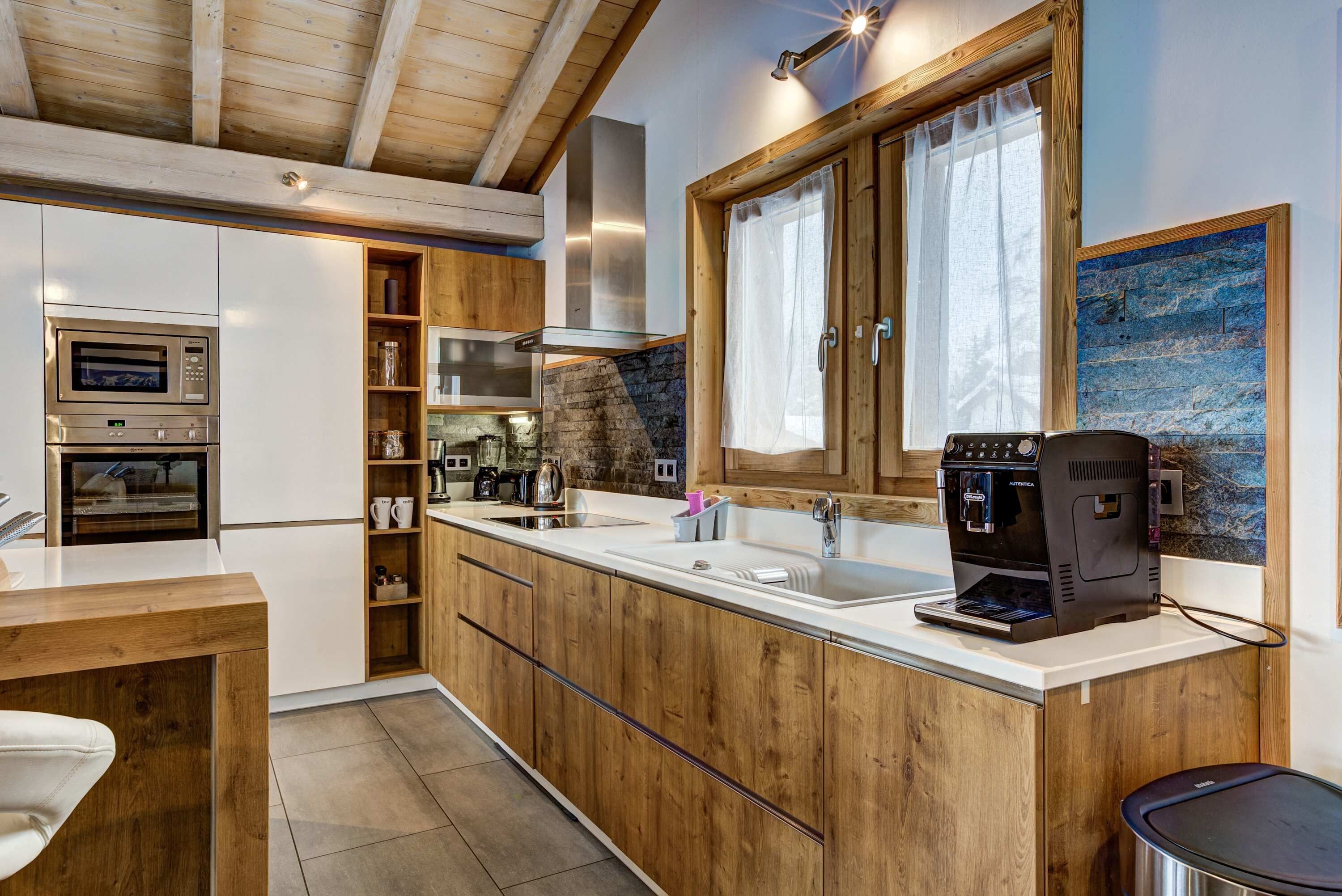 Una cucina moderna con mobili in legno, forno a incasso, macchina da caffè e un'ampia finestra con tende.