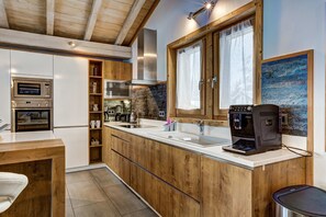 Una cocina moderna con armarios de madera, horno empotrado, cafetera y un ventanal con cortinas.