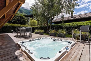 Una terraza de madera con un jacuzzi, muebles de exterior y plantas en macetas.
