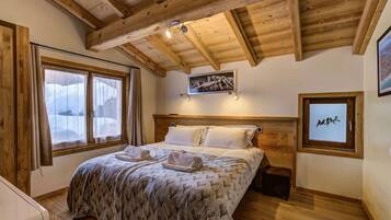 Una camera da letto con soffitto in legno, un letto con coperta a fantasia, due lampade ai lati del letto e un quadro appeso alla parete.