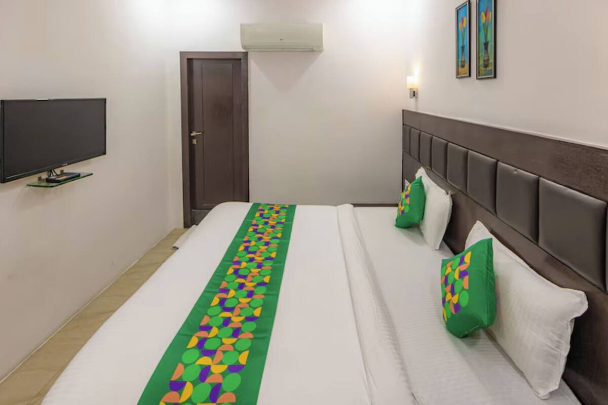 A hotel room with a bed, a television, a door, and a wall-mounted air conditioner.