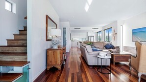 Amplia sala de estar con una escalera de madera, un espejo grande, un conjunto de sofás, una mesa de centro y un televisor.