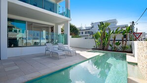 Un edificio residencial moderno con piscina, sillas de descanso y plantas tropicales.