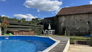 Una piscina con muelle de madera, pared de piedra y valla de madera.