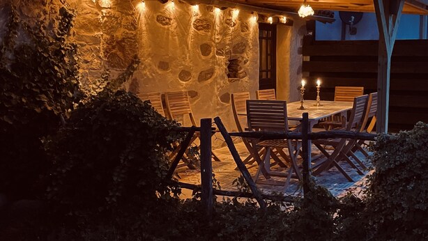 Un área de comedor al aire libre con paredes de piedra, muebles de madera y luces colgantes.