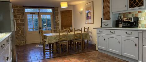 Una cocina con mesa de comedor, armarios blancos, pared de piedra y ventana.