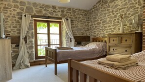 Un dormitorio con pared de piedra, una cama de madera, un aparador de madera y una ventana con cortinas.