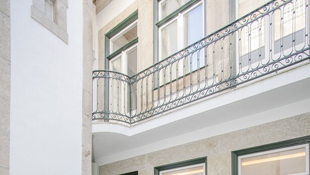 A courtyard with a table and chairs, a balcony, and a door leading to an interior space.