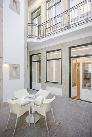 Ein Innenhof mit Tisch und Stühlen, ein Balkon und eine Tür zu einem Innenraum.