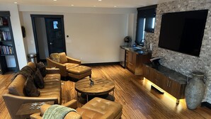 Un salon moderne avec des canapés en cuir, une table basse en bois et un coin cuisine doté d’un grand téléviseur et d’un revêtement mural en pierre.