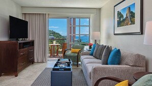 Ein Hotelzimmer mit einer Couch, einem Fernseher, einem Couchtisch, einem Sessel und einem Balkon mit Meerblick.