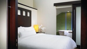 Ein Hotelzimmer mit Bett, Nachttisch mit Lampe, Blumenvase und Blick ins Bad.