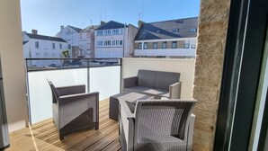 Een balkon met rieten meubilair, uitzicht op omliggende gebouwen en een houten vloer.