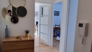 Een gang met een houten dressoir, een spiegel en een kleine plant. Een deur leidt naar een andere kamer.