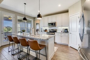 A modern kitchen with white cabinets, a large island with bar stools, stainless steel appliances, and pendant lighting.