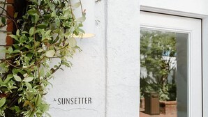 Een witte deur met een raam, een klein buitgedeelte met een bakstenen muur, en een label met de tekst 'The Sunsetter'.