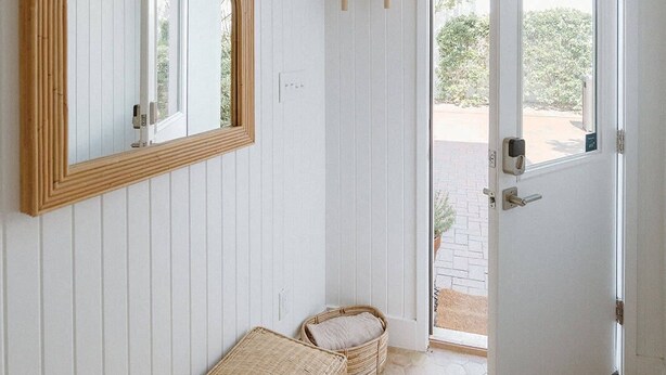 Een kamer met een houten bankje, een grote spiegel en een deur naar buiten.