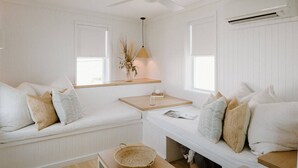 Een knus, wit ingerichte kamer met een bankje, een tafeltje en een mand.