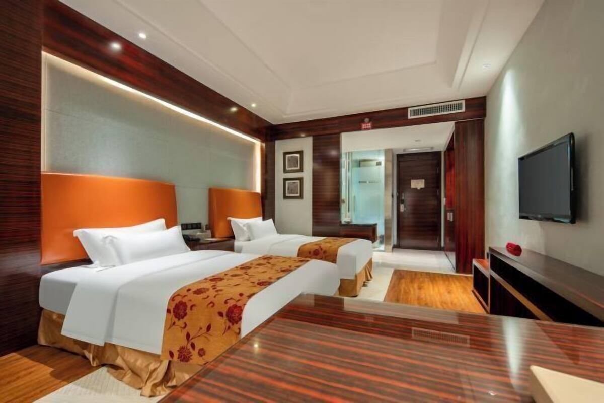 Ein Hotelzimmer mit zwei Betten, einem Fernseher, einem Schreibtisch und einem Spiegel.
