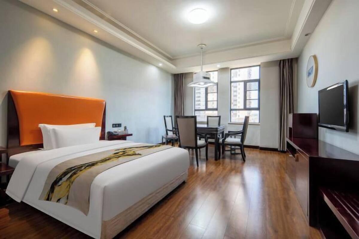 Ein Hotelzimmer mit einem großen Bett, einem Schreibtisch, einem Stuhl, einem Fernseher und einem Fenster mit Vorhängen.