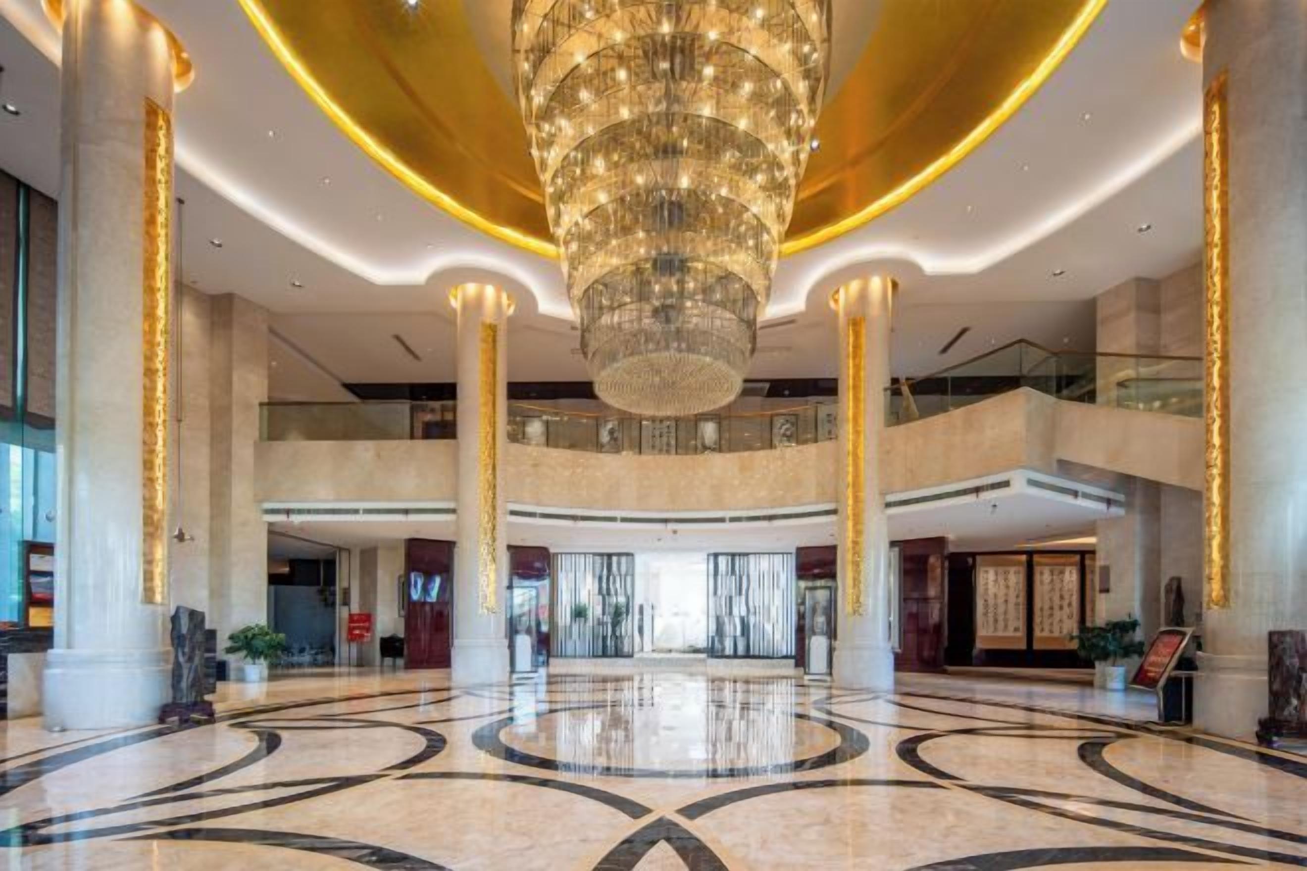 A spacious lobby with a large chandelier, high ceilings, and a polished marble floor.