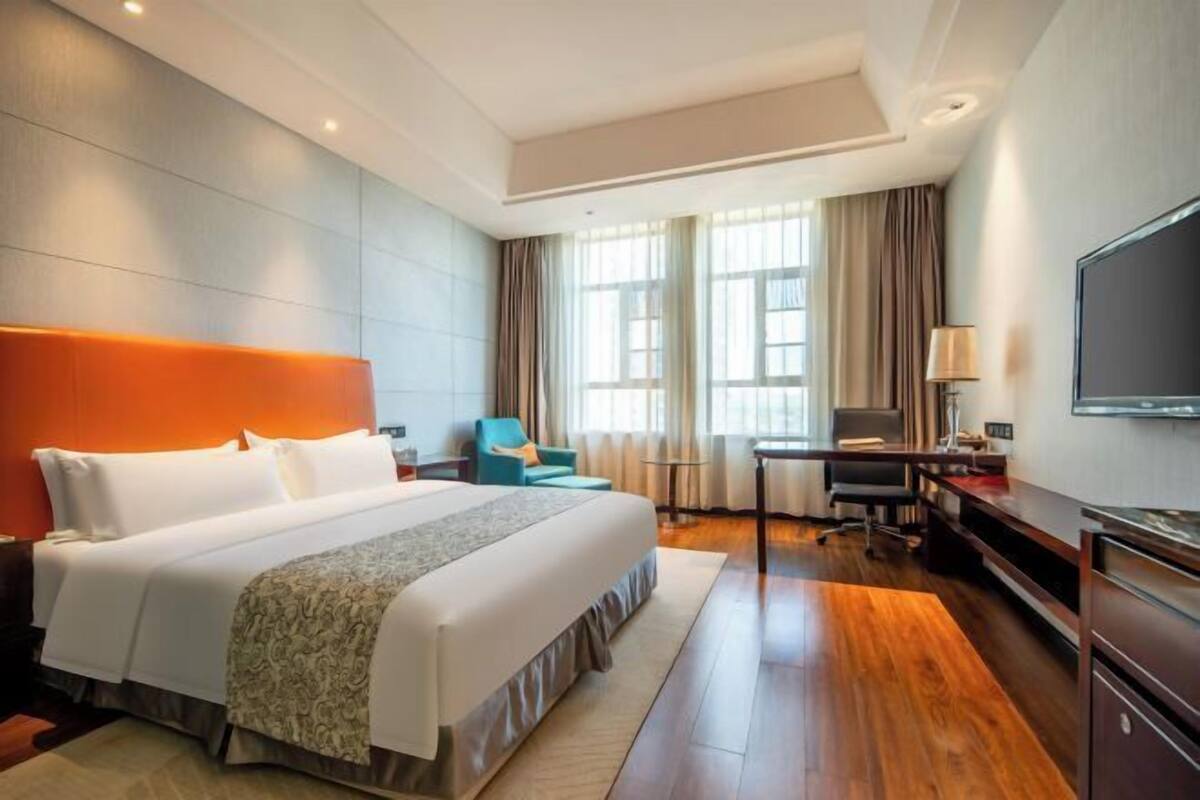 Ein Hotelzimmer mit einem großen Bett, einem Schreibtisch, einem Sessel, einem Fernseher und einem Fenster mit Vorhängen.