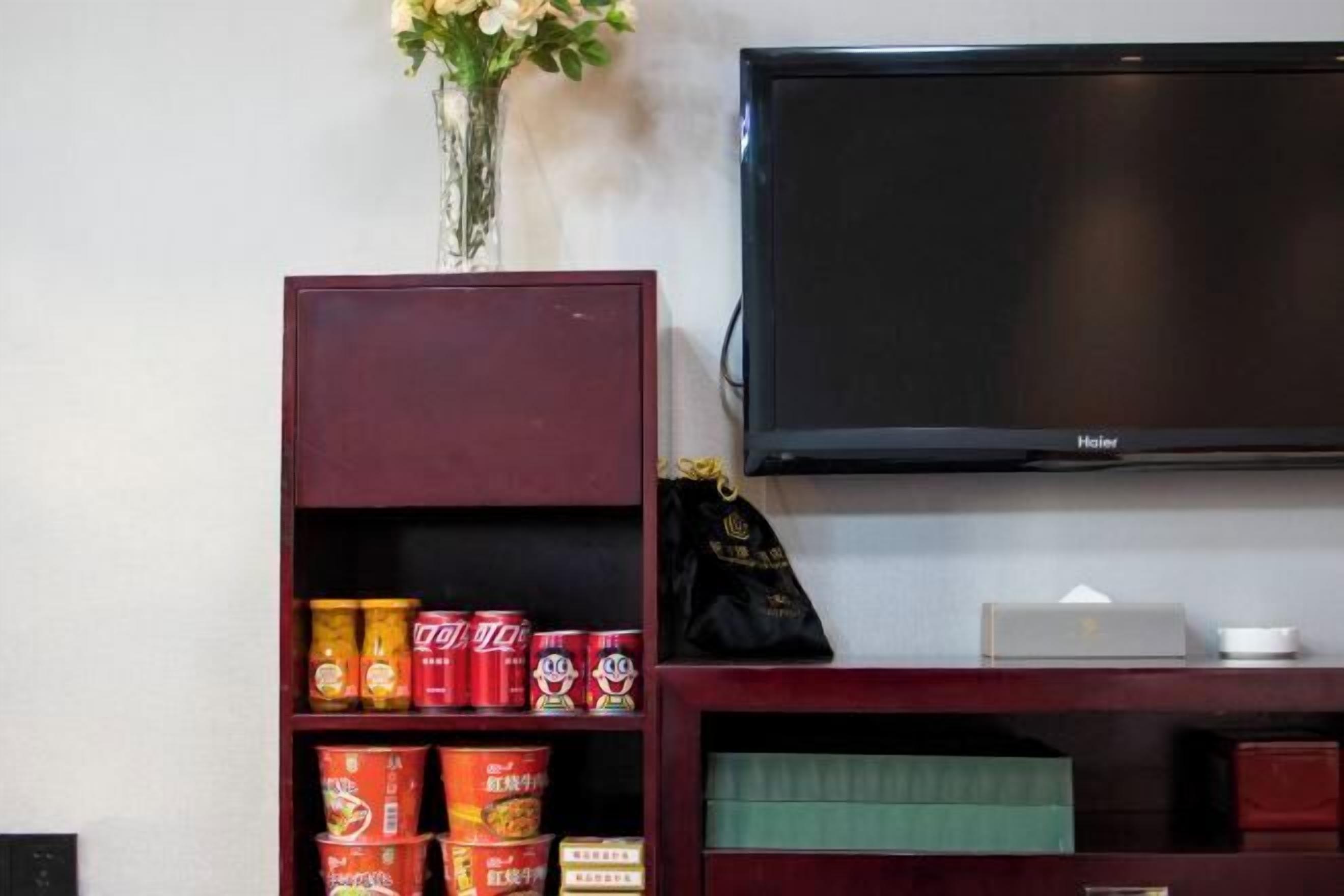 Une pièce avec un téléviseur fixé au mur, une étagère remplie de conserves et un vase avec des fleurs.