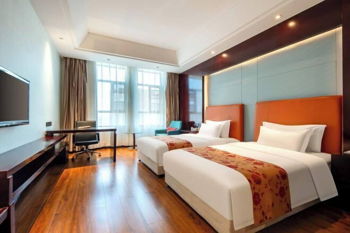 Ein Hotelzimmer mit zwei Betten, einem Schreibtisch, einem Fernseher und großen Fenstern.