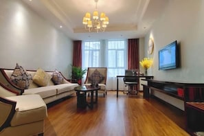 A modern living room with a sofa, armchair, coffee table, and a TV mounted on the wall. - Silverhall Grand Hotel (Qichun)