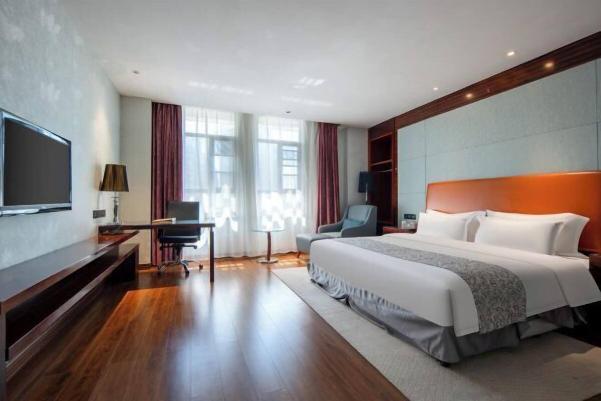 Ein Hotelzimmer mit einem großen Bett, einem Schreibtisch mit Stuhl, einem Fernseher und einem Kleiderschrank.
