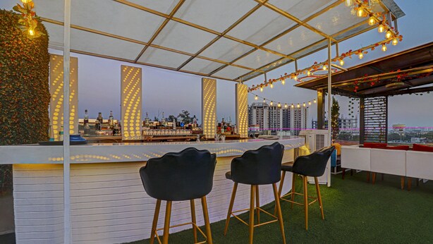 An outdoor bar area with a white counter, black bar stools, and string lights. - Treebo C1 Taj Nirvana (Agra)