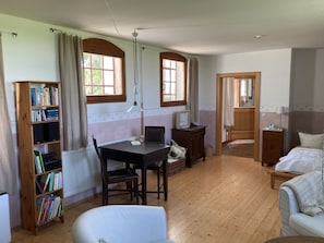 Une pièce avec un bureau en bois, des étagères, un fauteuil blanc, un lit et une fenêtre avec des rideaux.