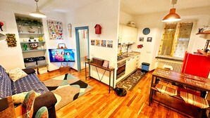 A cozy living room with a sofa, a coffee table, a TV, and a kitchen area with a stove and cabinets. - Meizon Genoa - 5 minutes from the station, the sea, the subway (Genova)