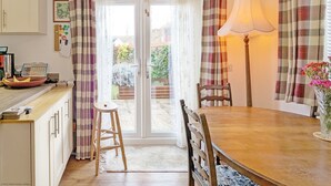 A cozy kitchen with a wooden table, chairs, a stool, a lamp, and a view through the glass door to the garden.