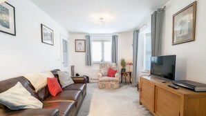 A living room with a leather sofa, a patterned armchair, a wooden cabinet, and a television.