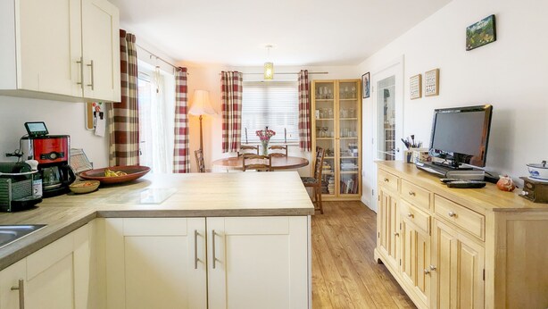 A compact kitchen with a coffee machine, a dining table with chairs, a television, and wooden cabinets.